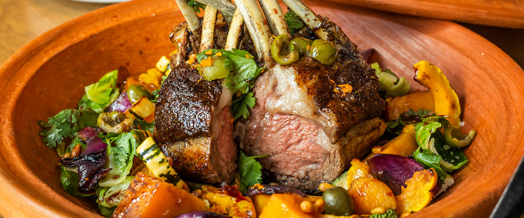 Plated Lamb Rack Tagline with seasonal squash, apricots, green olives, couscous and roasted chili lemon relish.