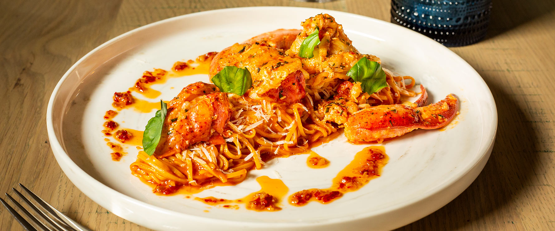 Plated Lobster Spaghetti with large pieces of lobster atop sweet garlic tomato sauce, parmigiana reggiano and Calabrian chili.