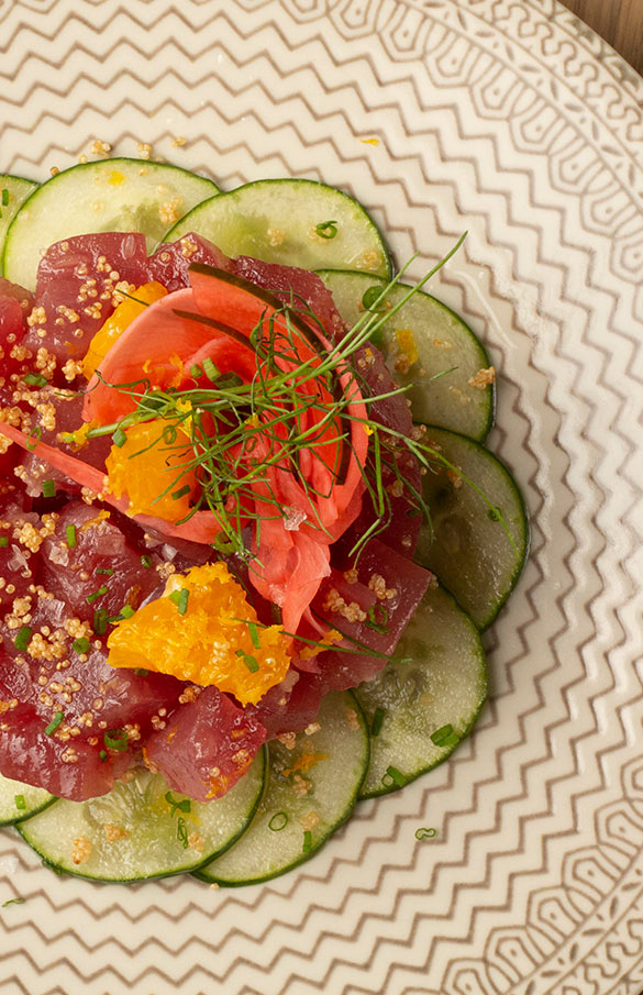 Yellowfin Tuna Tartare arranged on overlapping circles of sliced cucumber with orange oil and pickled vegetables.