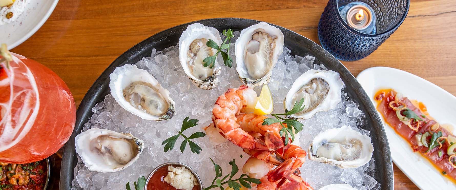 Bird's eye view of iced bowl with shrimp and shucked oysters next to beverages