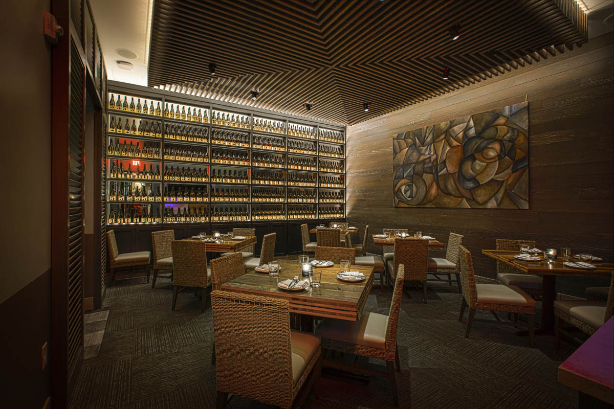 Interior dining room with wall of wine bottles at night at Del Mar restaurant in Naples, Florida