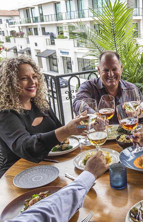 Couple toasting with friends at outdoor table at Del Mar Mediterranean restaurant in Naples, Florida.