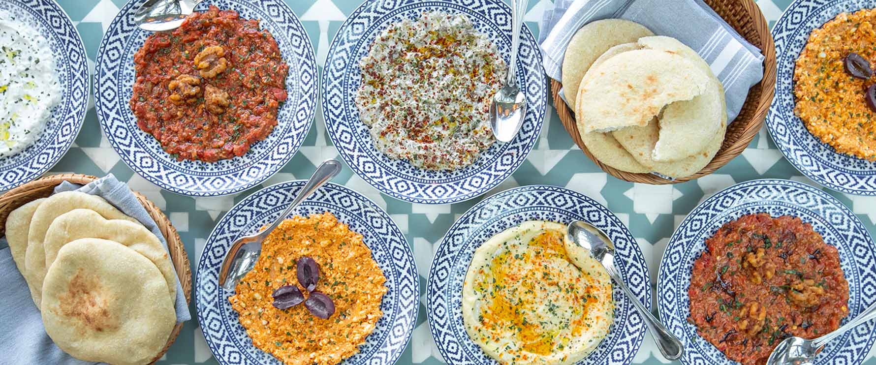 A large spread of mediterranean food from Del Mar Mediterranean sits on a patterned tablecloth.